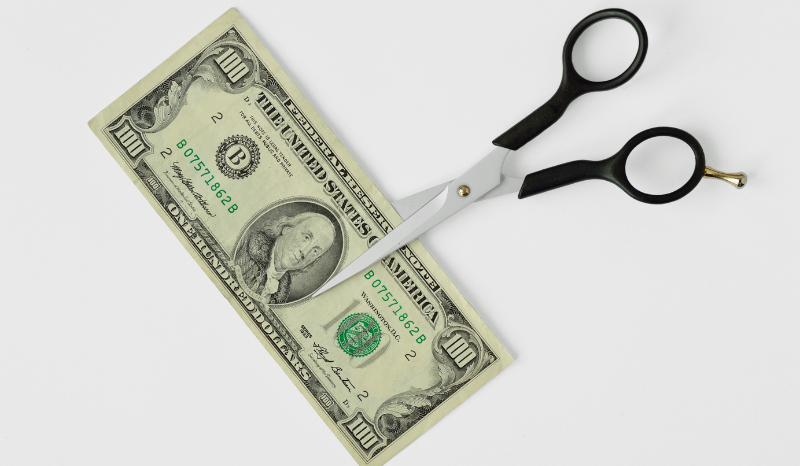 An image of a pair of scissors cutting a 100 dollar bill