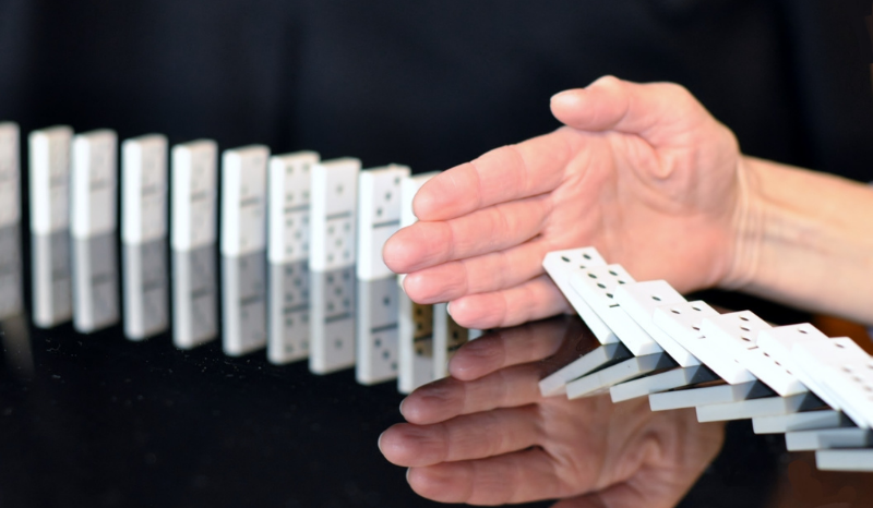Image of falling dominoes blocked in mid-stream by a hand.
